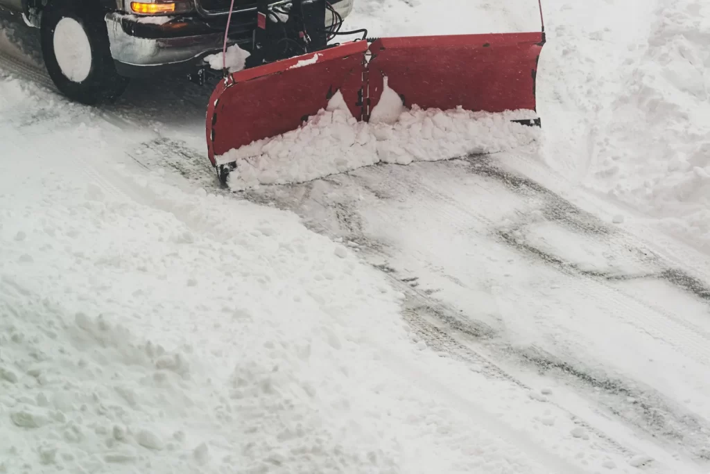 Red snowplow blade pushing snow across a road